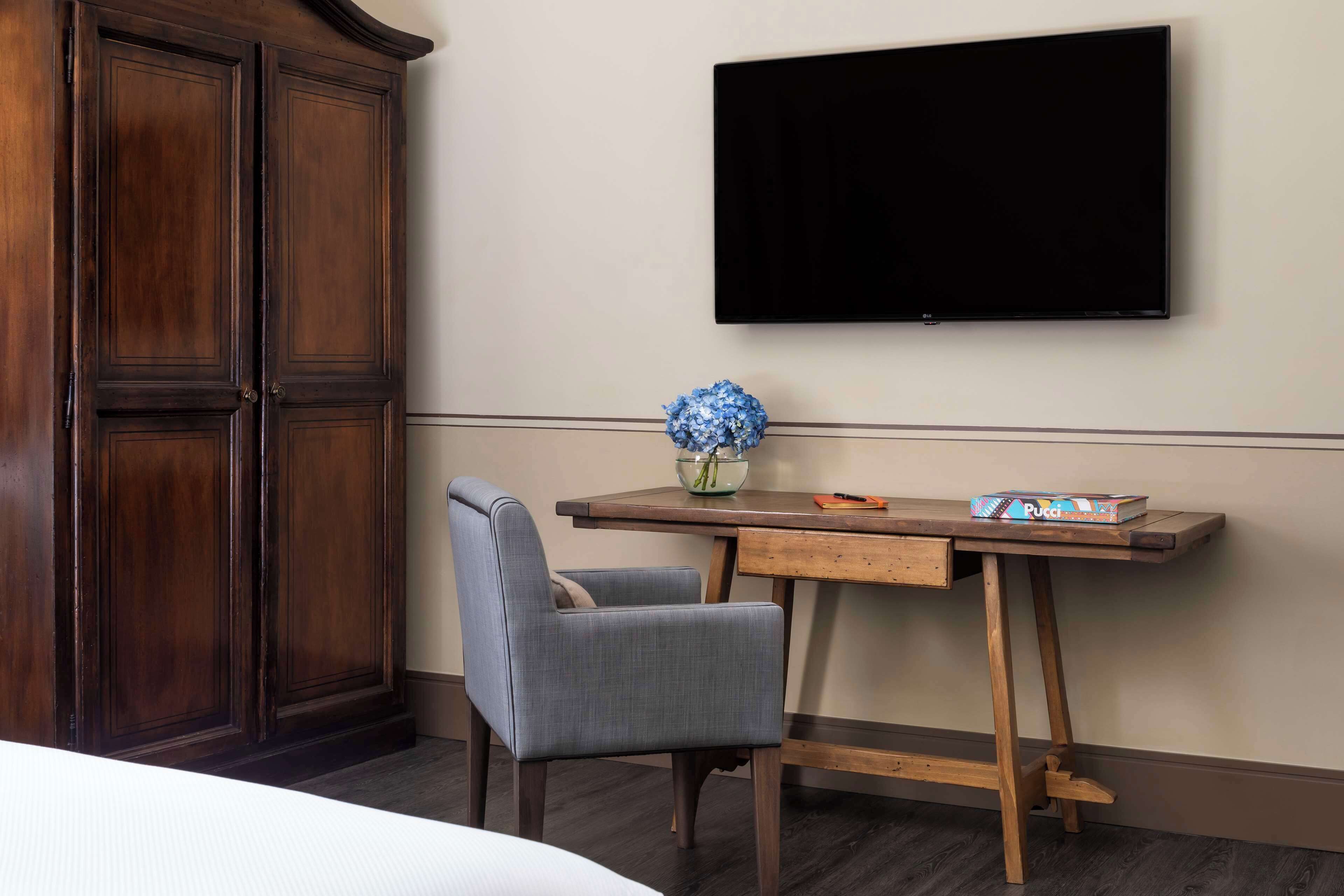 Una camera d'albergo con una scrivania in legno, una sedia, una TV a schermo piatto e un armadio.