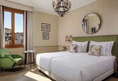 A hotel room with a large bed, a green armchair, a small table, and a window with curtains.