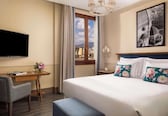 A hotel room with a bed, a desk, a chair, a TV, a window with curtains, and a cityscape view.