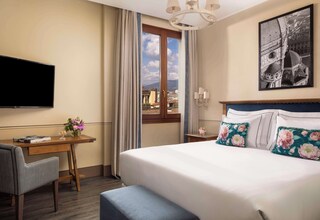 A hotel room with a bed, a desk, a chair, a TV, a window with curtains, and a cityscape view.