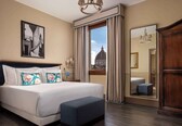 A hotel room with a large bed, a view of a dome through a window, a mirror, and a wooden wardrobe.