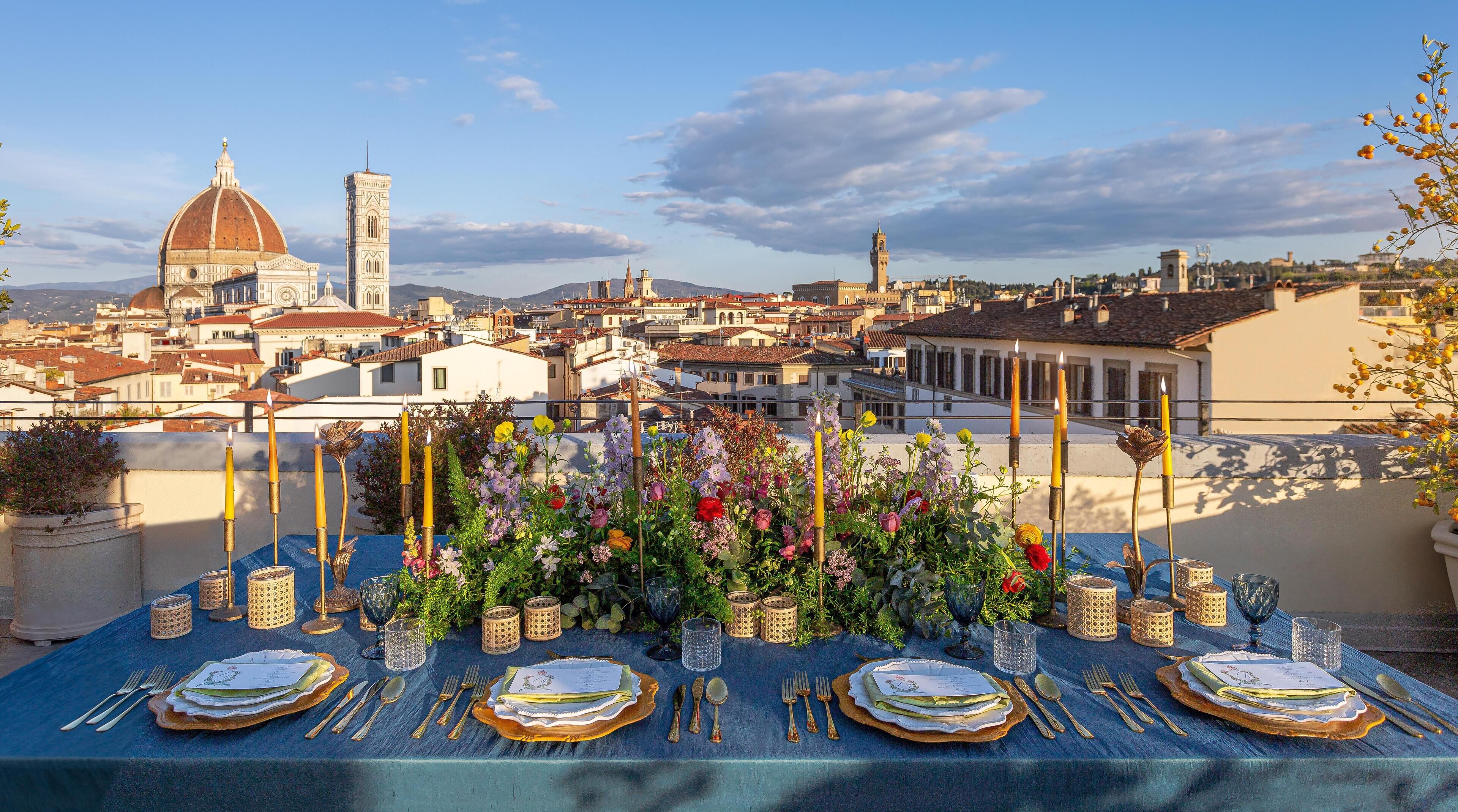 A rooftop dining table set with a view of historic buildings and a dome in the background.