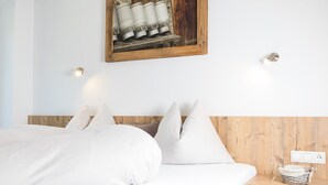 A bedroom with a wooden headboard, white bedding, a small bedside table with a basket, and a wall-mounted light fixture. - Hieserhof (Neustift Im Stubaital)