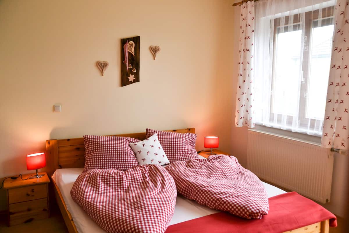 A double bed with checkered bedding, two bedside tables with lamps, a wall clock, and heart-shaped decorations.
