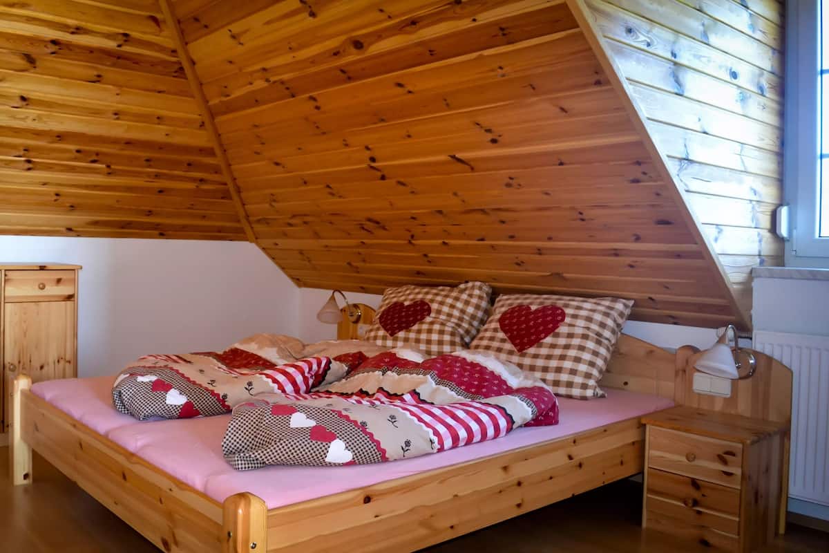 A wooden bed with a sloped ceiling, checkered bedding, and heart-shaped pillows.