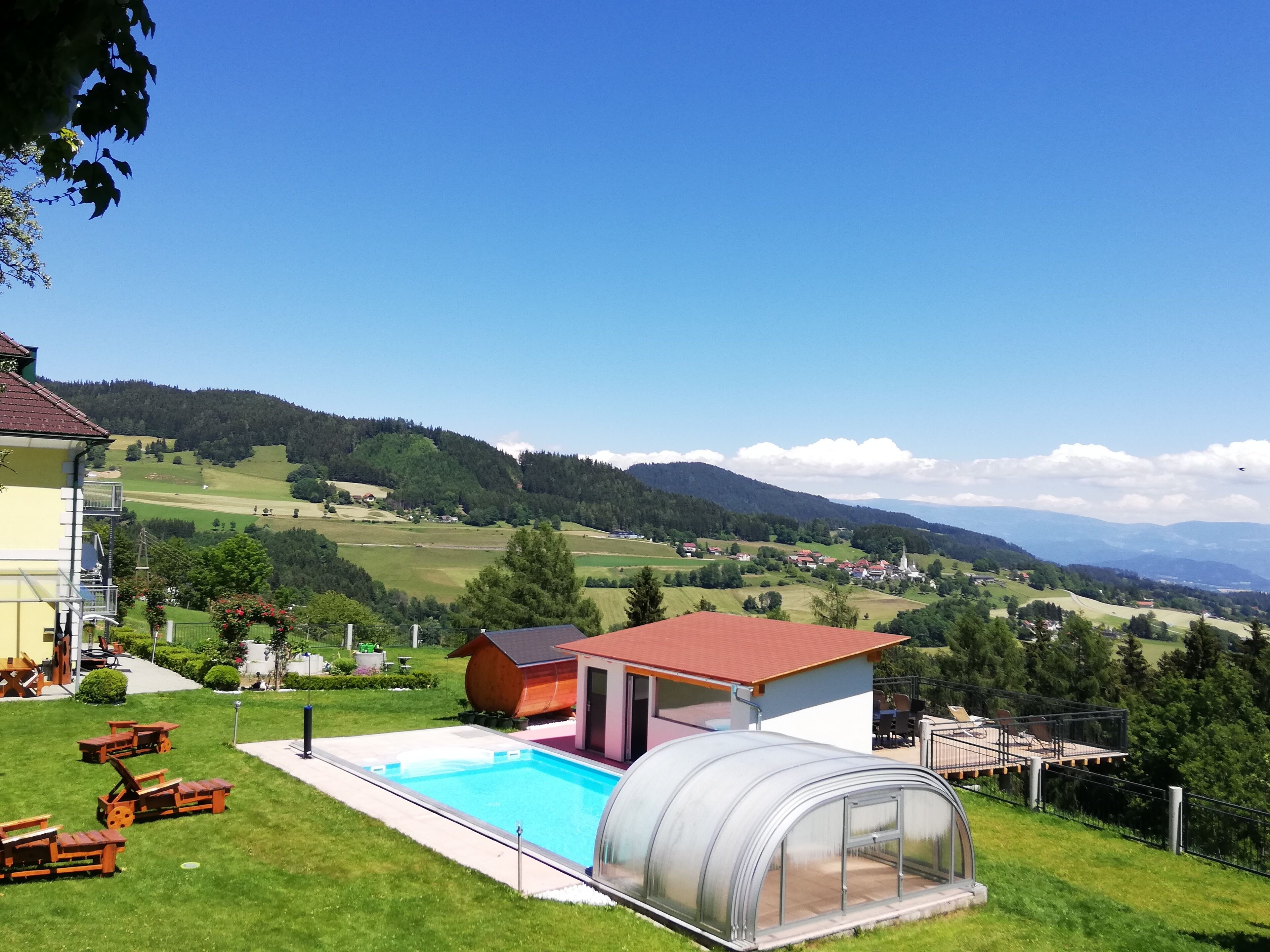 Um imóvel residencial com piscina, estufa e vista para uma paisagem rural com montanhas.