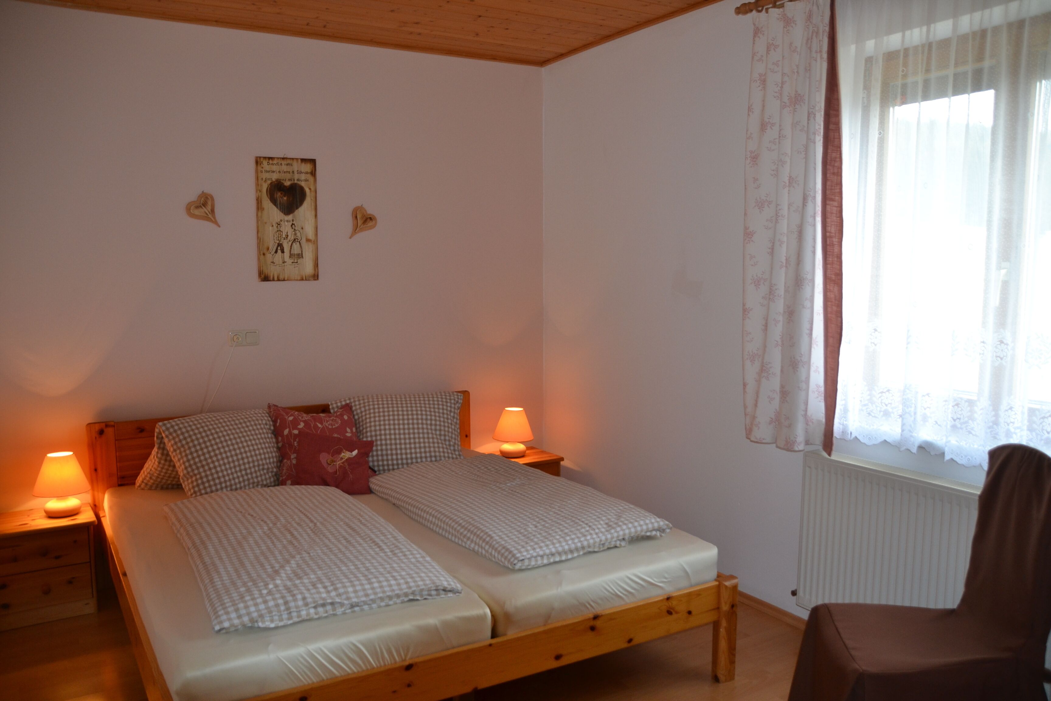 A bedroom with a wooden bed, two bedside tables with lamps, a radiator, and a window with curtains.