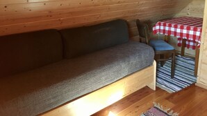 Un interior de madera con un sofá, una mesita con mantel a cuadros y una silla.