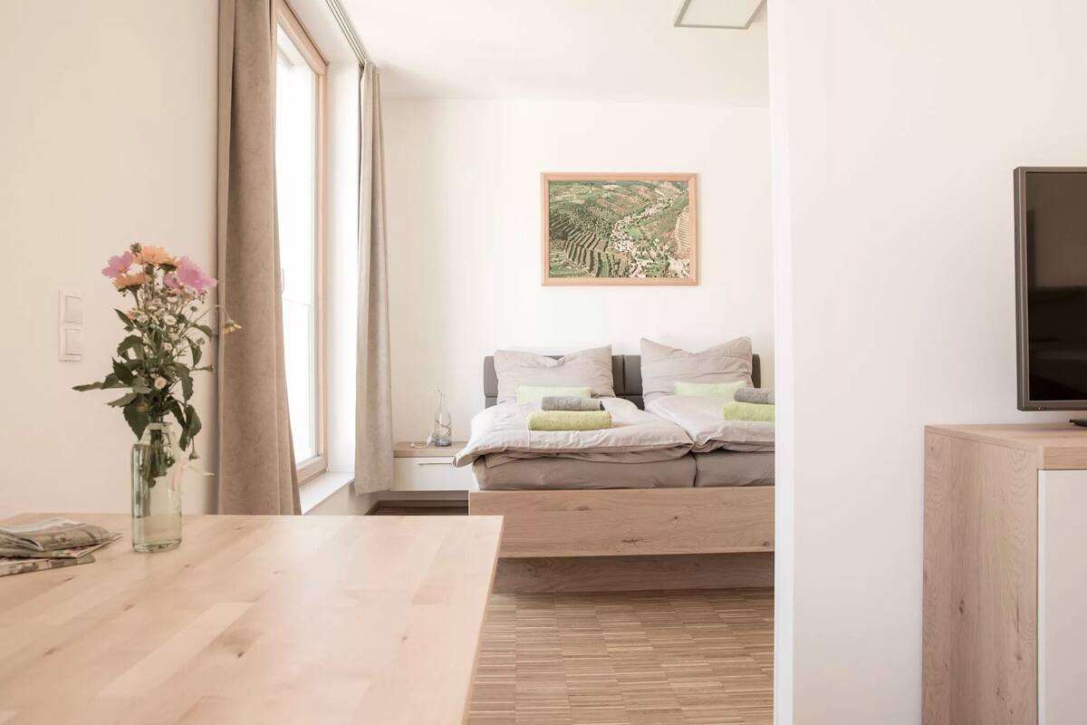 Un dormitorio moderno con cama, televisor, mesa de madera y ventana con cortinas.