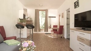 Un salon moderne comprenant un canapé, une table basse agrémentée de fleurs, un téléviseur et un coin cuisine avec une table à manger et des chaises.