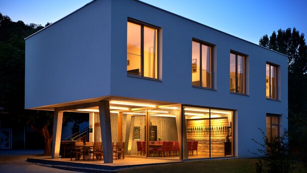 Une maison moderne à deux étages dotée d’un patio couvert, de grandes fenêtres et d’un espace de rangement pour les bouteilles de vin bien visible.