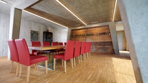 Une salle de conférence moderne avec une table en bois et des chaises rouges, un mur en bois orné de bouteilles et un plafond en béton.