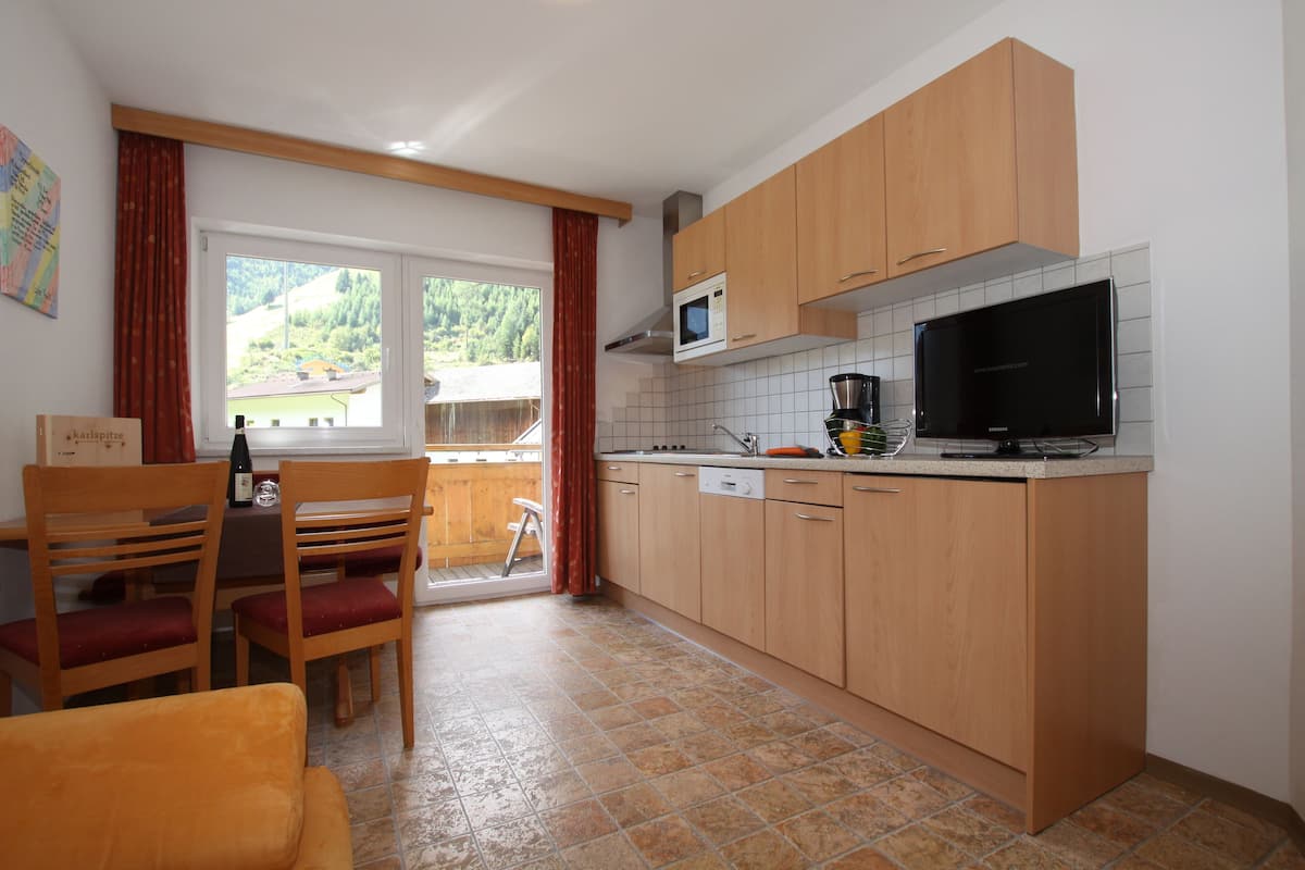Cocina compacta con armarios de madera, microondas, cafetera y televisor.