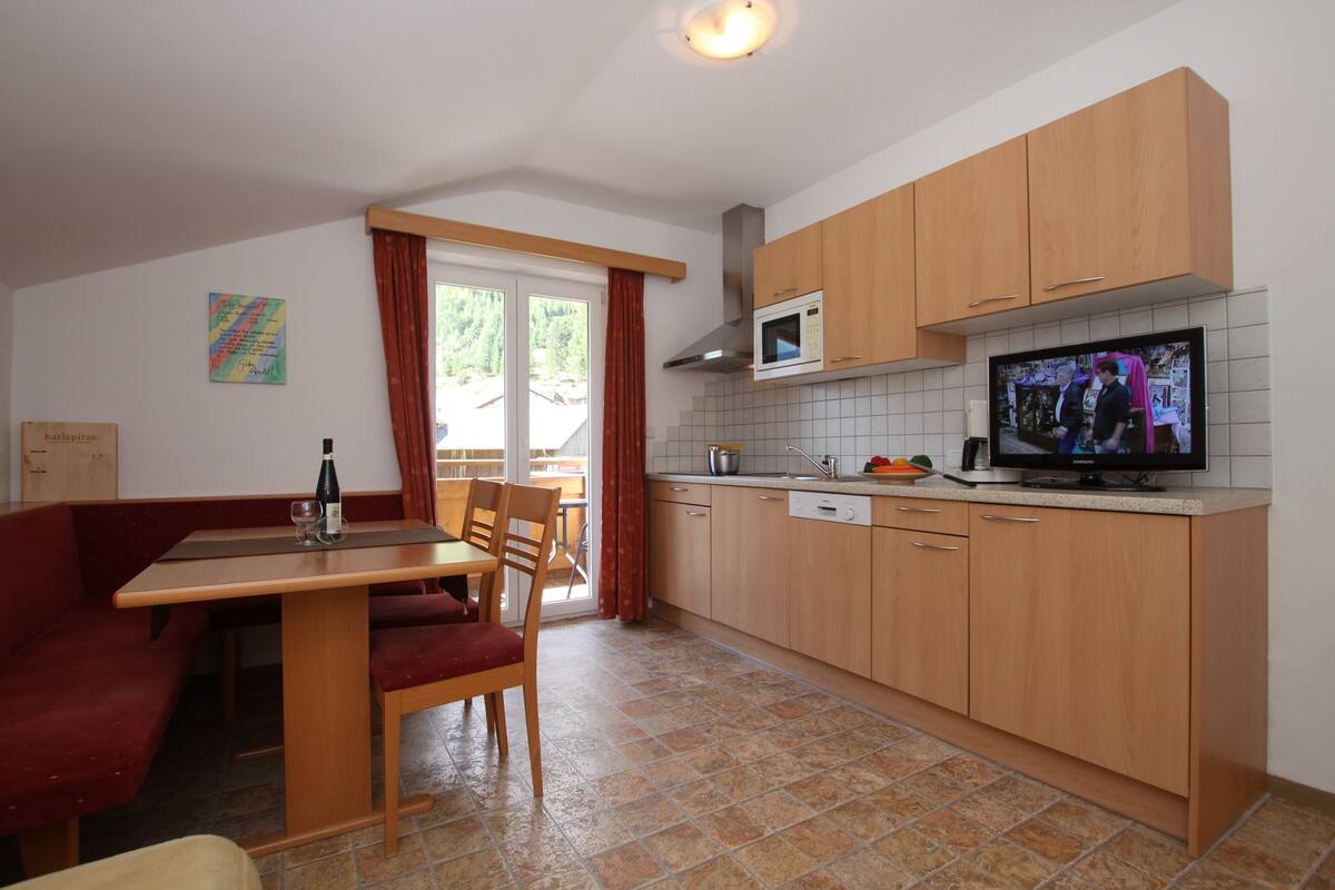 Cocina compacta con armarios de madera, microondas y comedor con mesa y sillas.