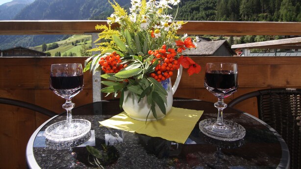 Una mesa con un florero y dos copas de vino en un balcón con vista a la montaña.