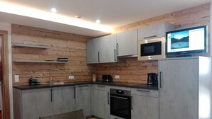 Una cocina moderna con armarios grises, horno empotrado, microondas y un televisor encima de la nevera.