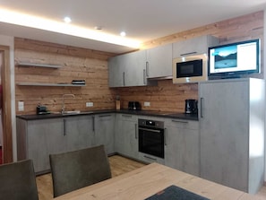 A modern kitchen with grey cabinets, a built-in oven, a microwave, and a television on top of the fridge.