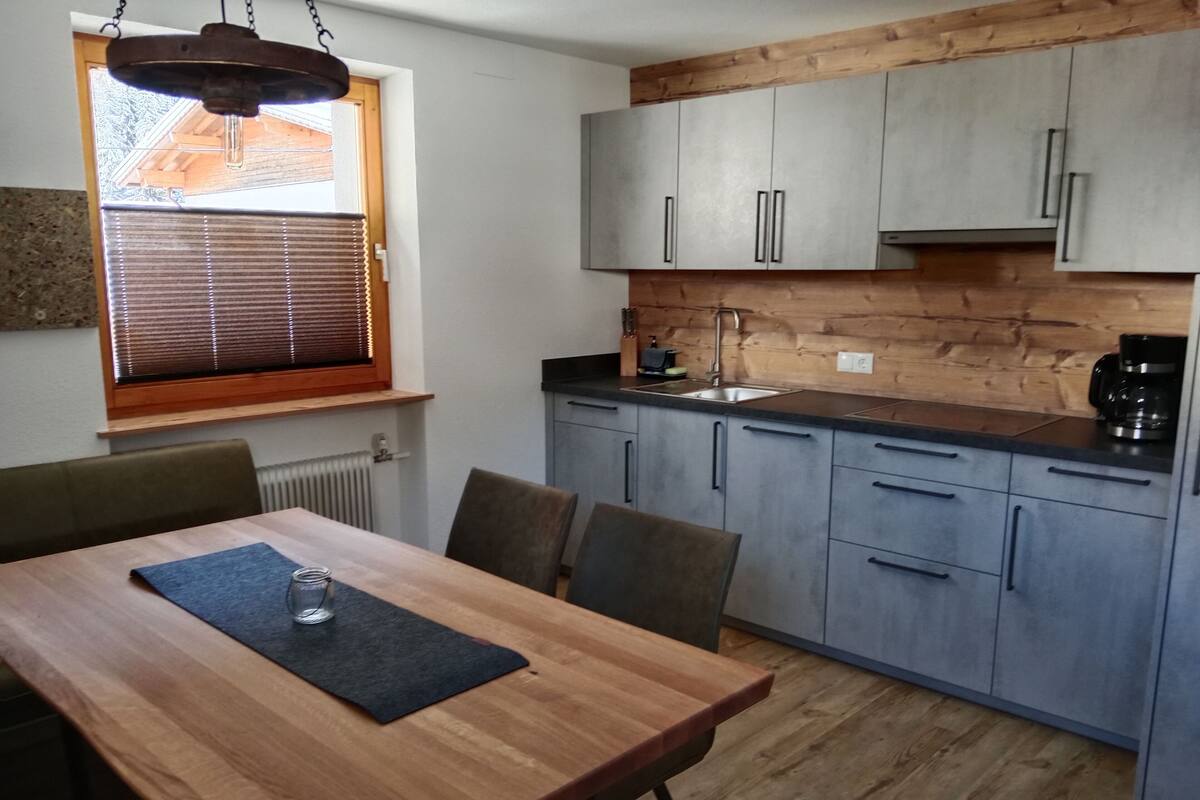 Una cocina moderna con armarios grises, encimera de madera y una ventana con persianas.