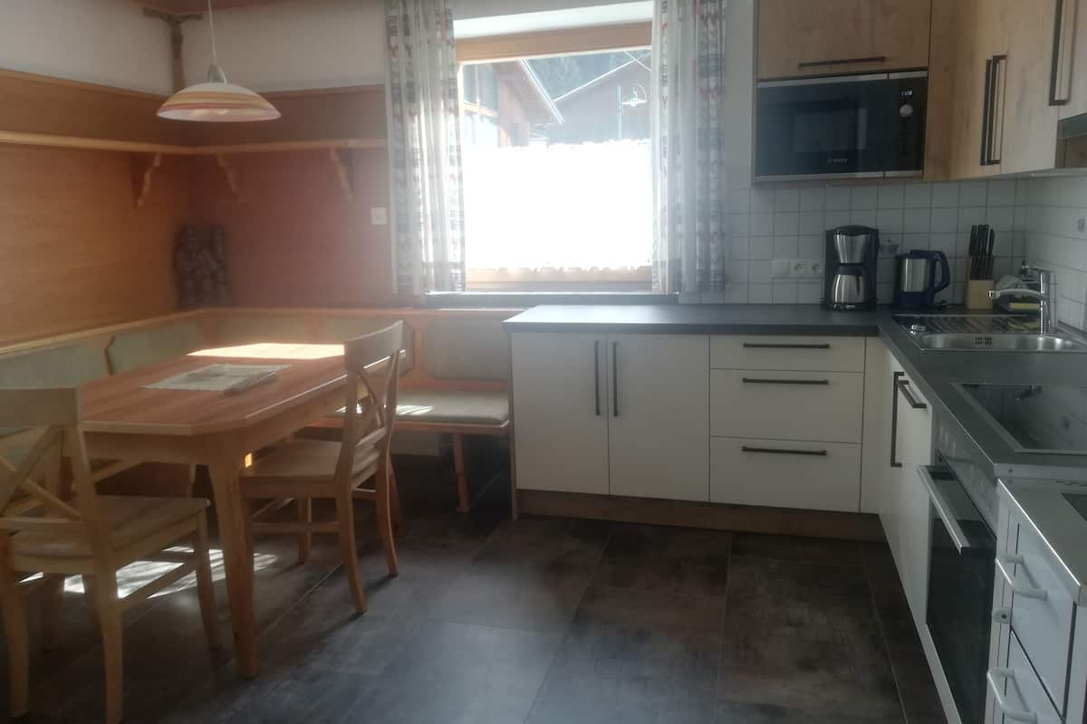 Una cocina con mesa, sillas, microondas, cafetera y alacenas.