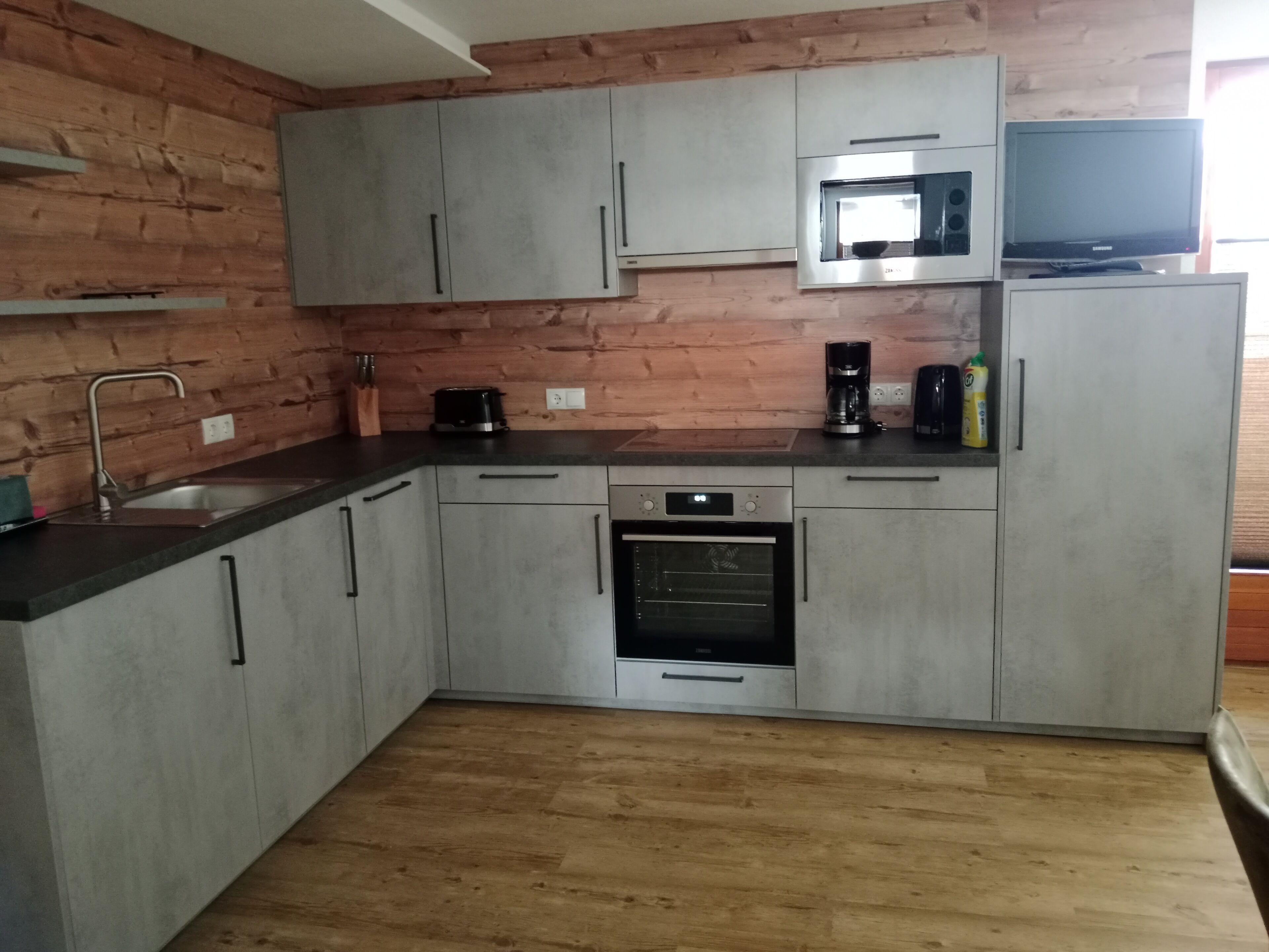 A modern kitchen with grey cabinets, a built-in oven, a microwave, and a coffee maker.