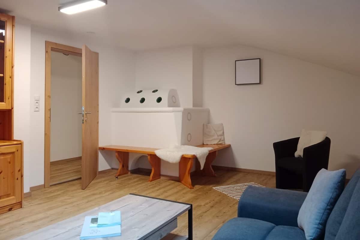 Una sala de estar con un sofá azul, un banco de madera, un armario blanco y un calentador blanco fijado a la pared.