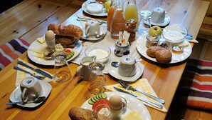 Mesa de madera dispuesta para el desayuno, con pan, huevos, queso y bebidas.