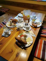 A wooden dining table set with breakfast items including bread, eggs, cheese, and beverages.