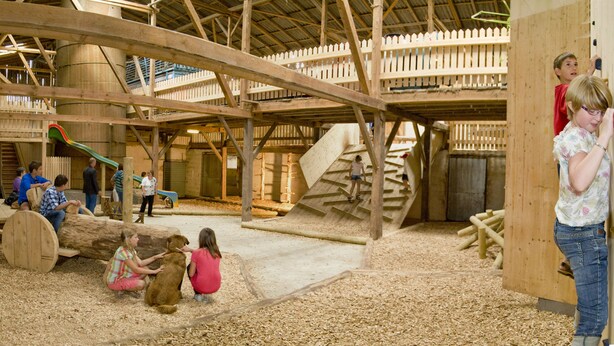 Zona de juegos de madera con toboganes y un tronco para que se sienten los niños.