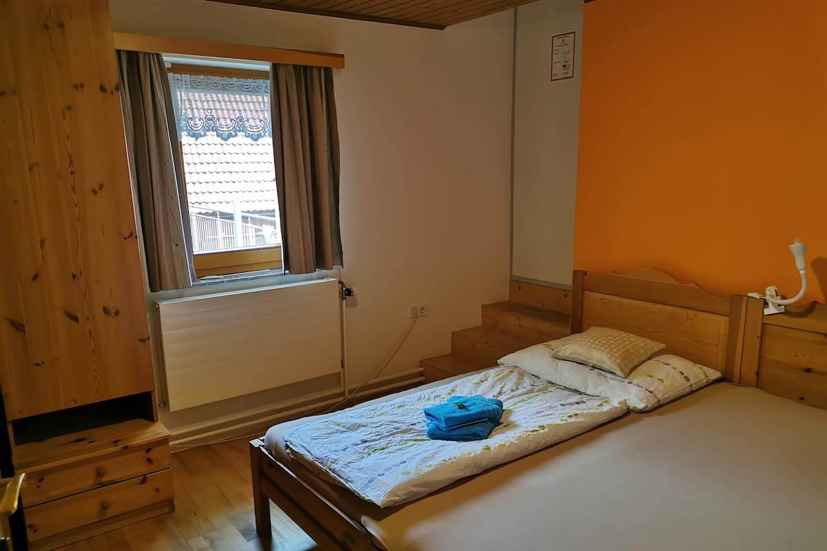 A bedroom with a wooden bed, a window with curtains, a radiator, and a wooden dresser.