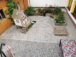 A courtyard with a wooden playhouse, a small table with chairs, and potted plants.