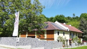 A two-story house with a stone wall, solar panels, and a flag. - Ferienwohnung Heimberger (Purgstall an der Erlauf)