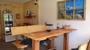 A rustic wooden dining table with benches, a guitar, and a bicycle in a cozy room with a large window displaying a scenic view. - Ferienwohnung Heimberger (Purgstall an der Erlauf)