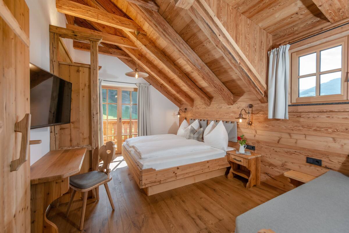 A wooden cabin bedroom with a bed, a desk, a chair, and a TV.