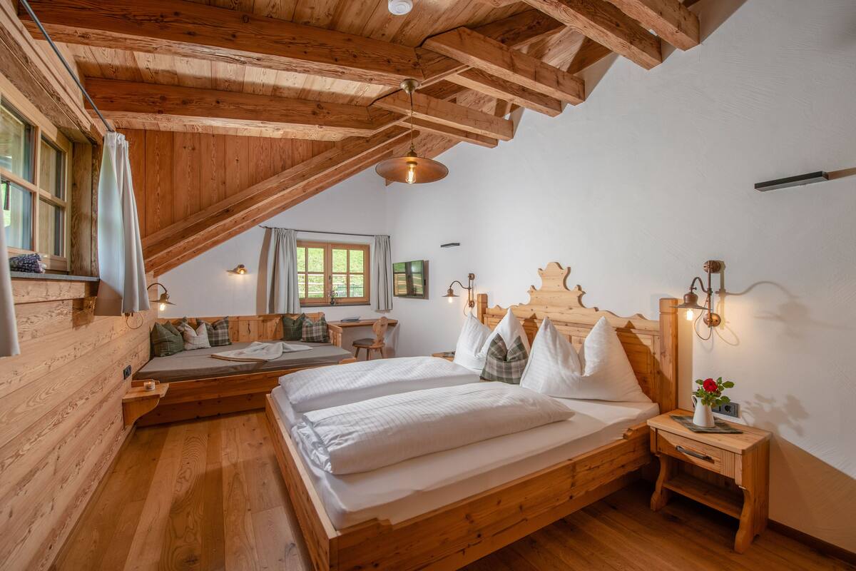 A wooden cabin bedroom with a loft bed, a small desk, and a window overlooking the outdoors.