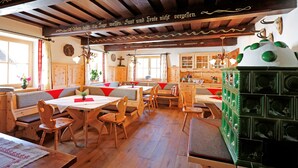 A traditional wooden interior with wooden benches and tables, a kitchen area with cabinets, and a decorative green cabinet. - Linharterhof Zimmer (Haus)