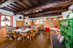 A traditional inn with wooden beams, a central seating area with benches and tables, and a green cabinet with glassware. - Linharterhof Zimmer (Haus)