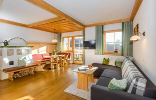 A cozy living room with a wooden ceiling, a sofa, a dining table, and a TV.