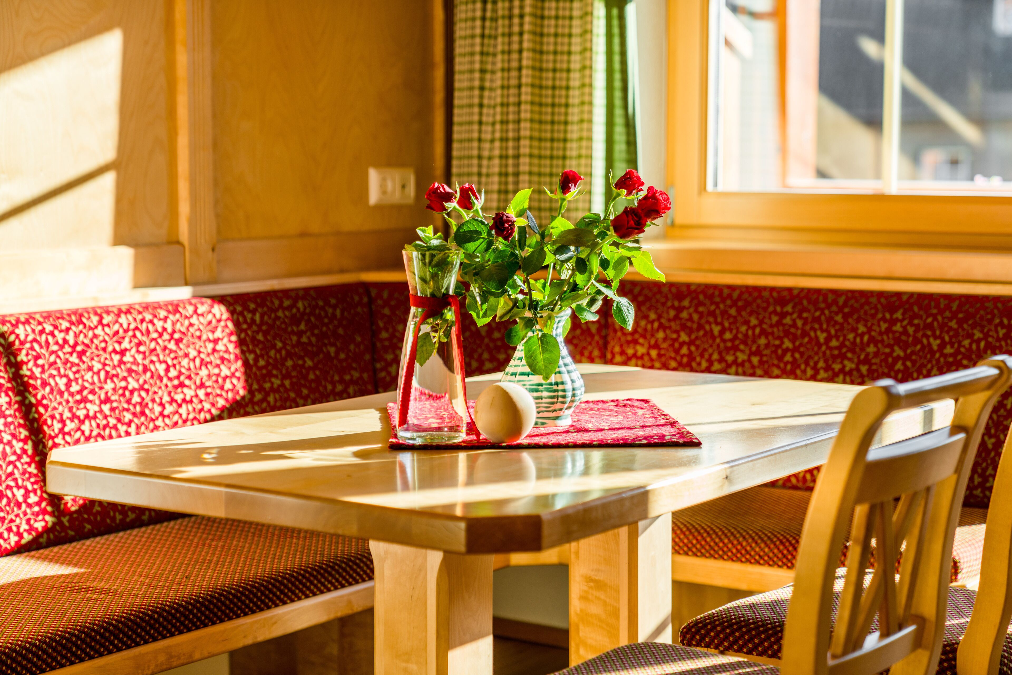Una mesa de madera con un jarrón de rosas rojas y un florero de vidrio con una sola flor blanca.