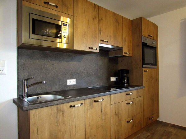 A modern kitchen with wooden cabinets, stainless steel appliances, and a black countertop.