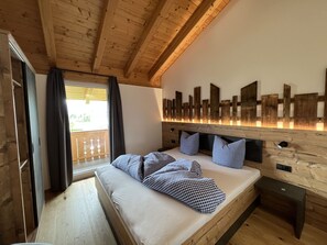 A wooden cabin bedroom with a bed, checkered pillows, a wooden headboard, and a balcony with curtains. - Studlerhof (Oberperfuss)