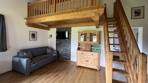 A loft-style room with a wooden staircase, a built-in wooden cabinet, and a grey sofa. - Studlerhof (Oberperfuss)