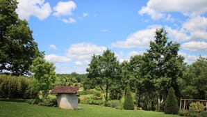 Um jardim exuberante com uma pequena construção de pedra, rodeado por árvores e um céu azul límpido.