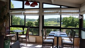 Uma sala de jantar com janelas amplas, uma mesa posta para dois e cadeiras.