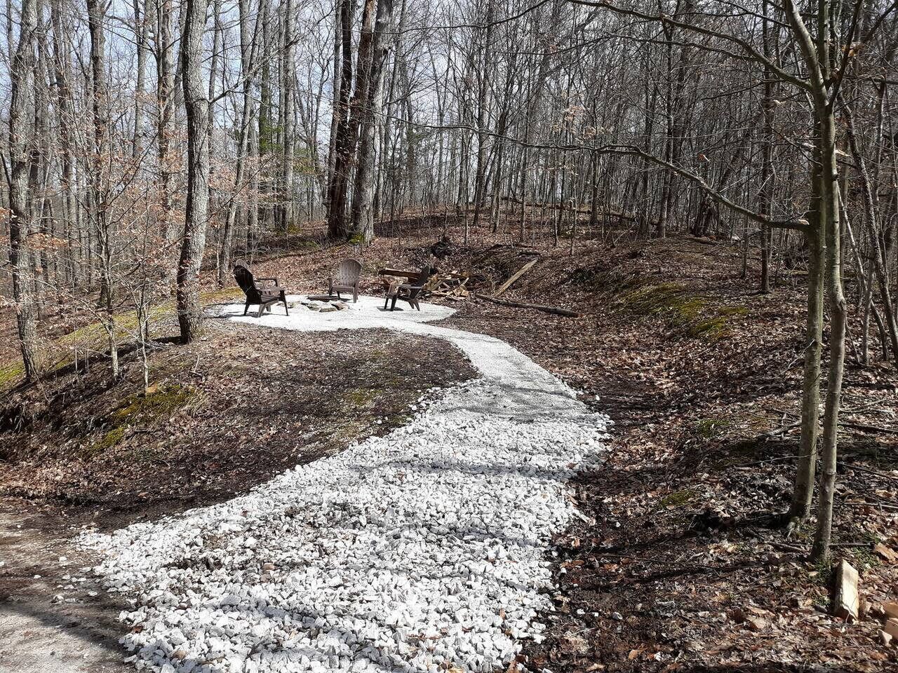 Un sendero de grava en una zona boscosa con bancos y una mesa de picnic.