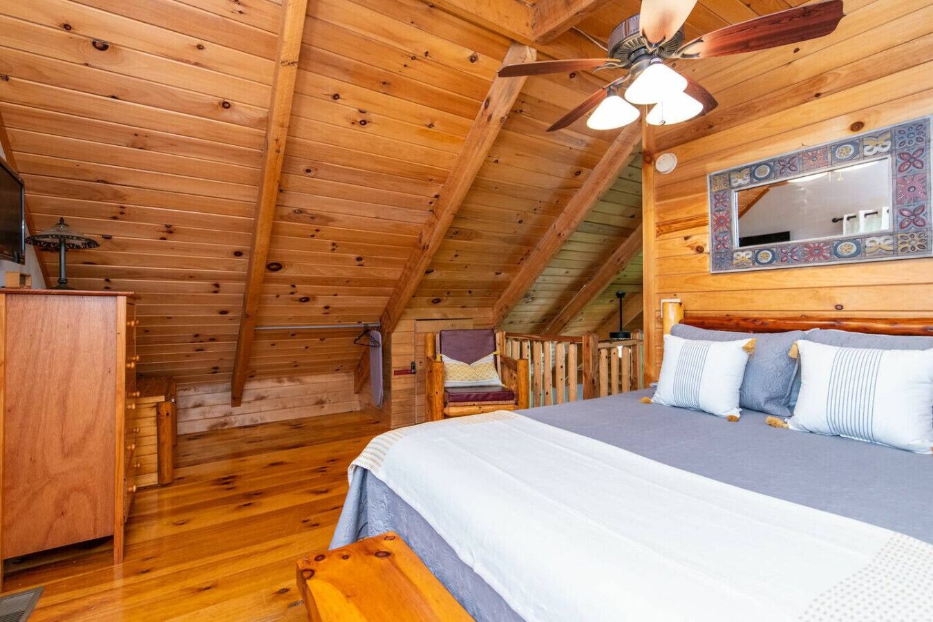 A cozy attic bedroom with a wooden ceiling, a bed with pillows, a chair, and a small table.