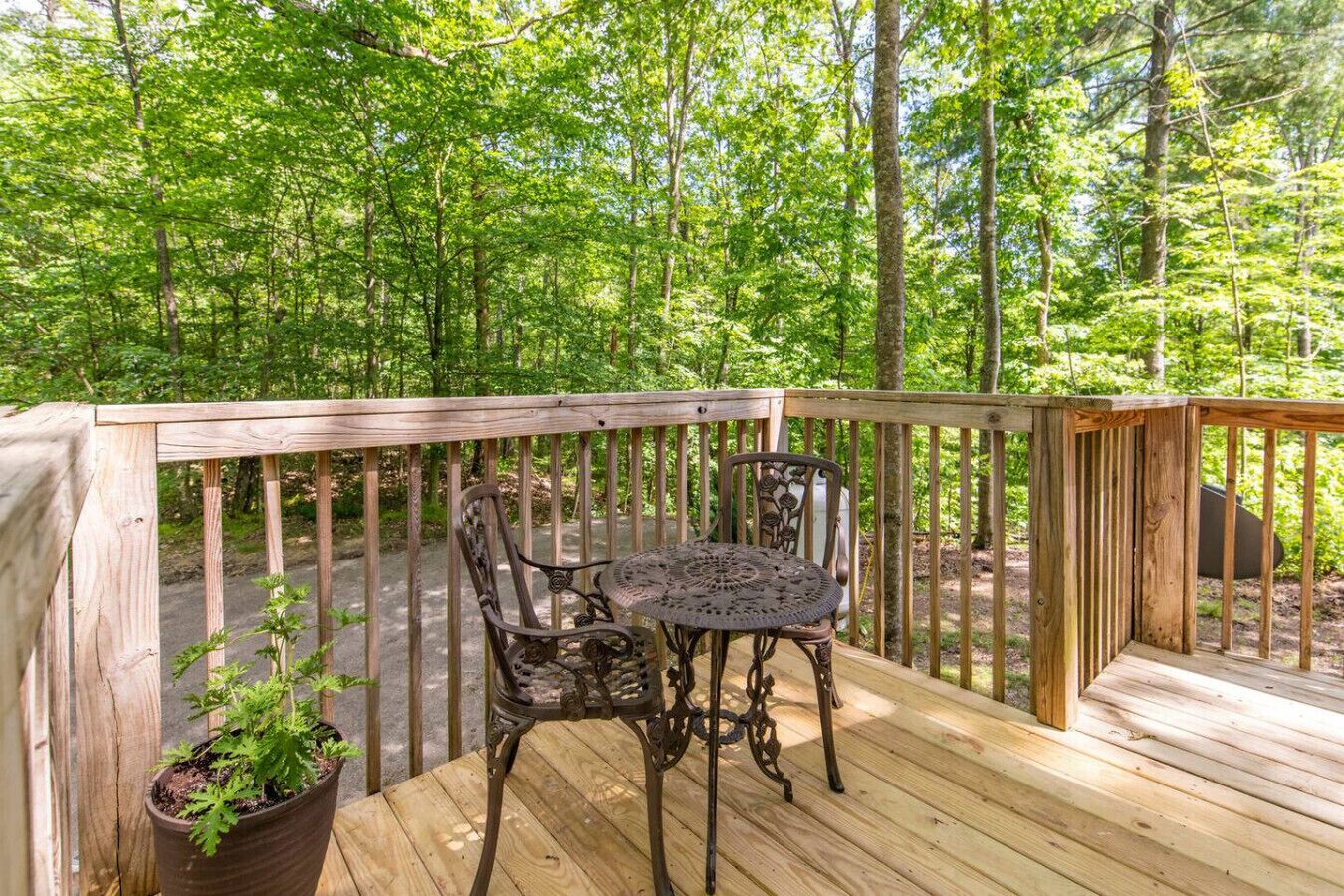 A wooden deck with a metal table and chairs, surrounded by a forested area.