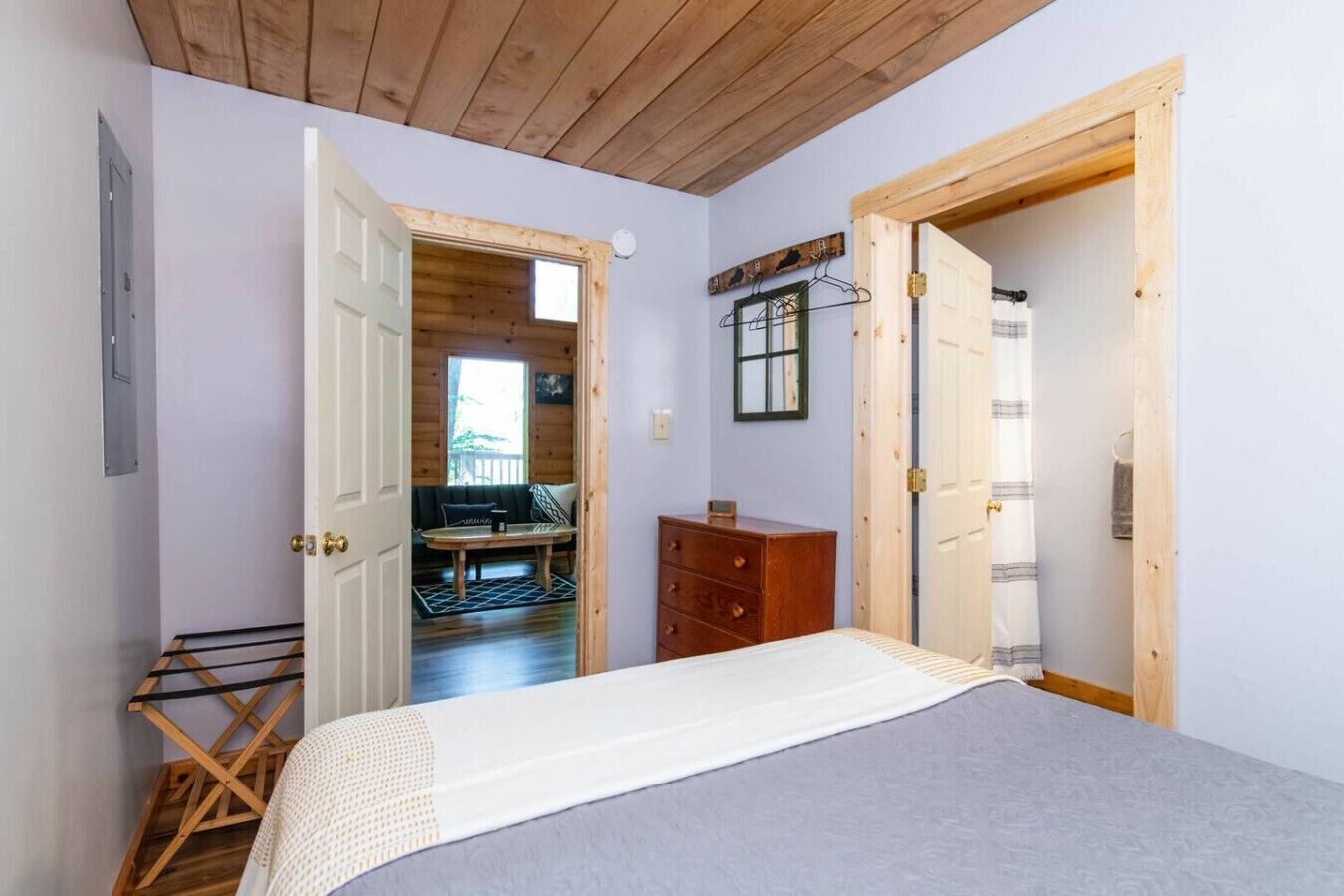 A bedroom with a bed, a wooden dresser, and a hanging rack.