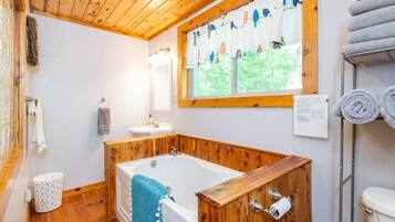 Une salle de bain avec une baignoire en bois, un lavabo, un miroir et une fenêtre avec des rideaux.