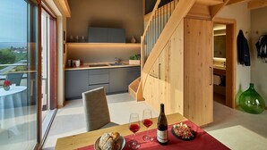 A modern kitchen with a wooden staircase, a dining area with a table set for two, and a view through large windows. - The key to more freedom (Eppan an der Weinstrasse)