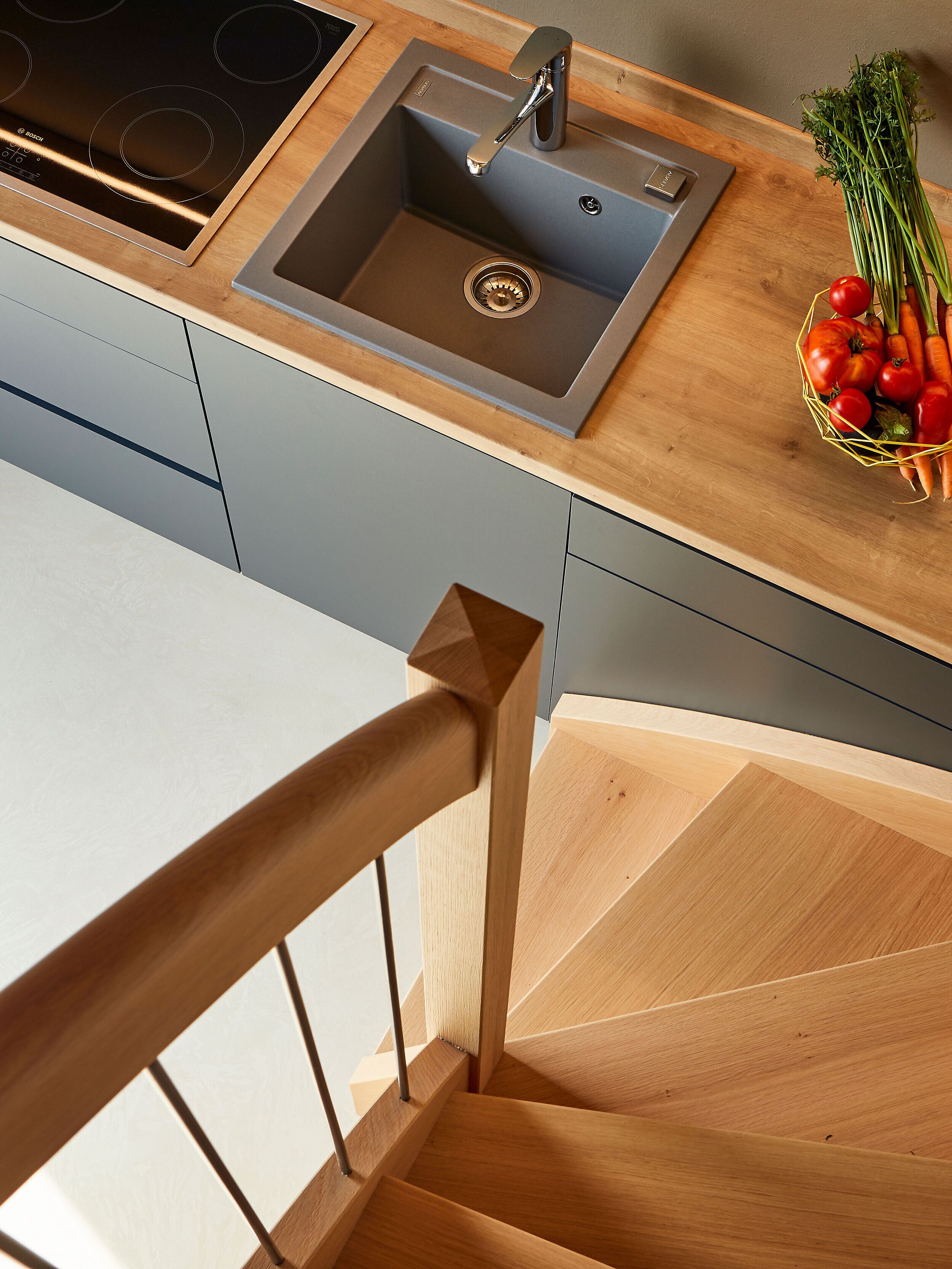 Une cuisine moderne dotée d’un évier en acier inoxydable, d’un plan de travail en bois et d’un escalier en bois.